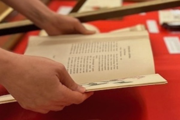 Hands carefully hold open a vintage book on a red display table